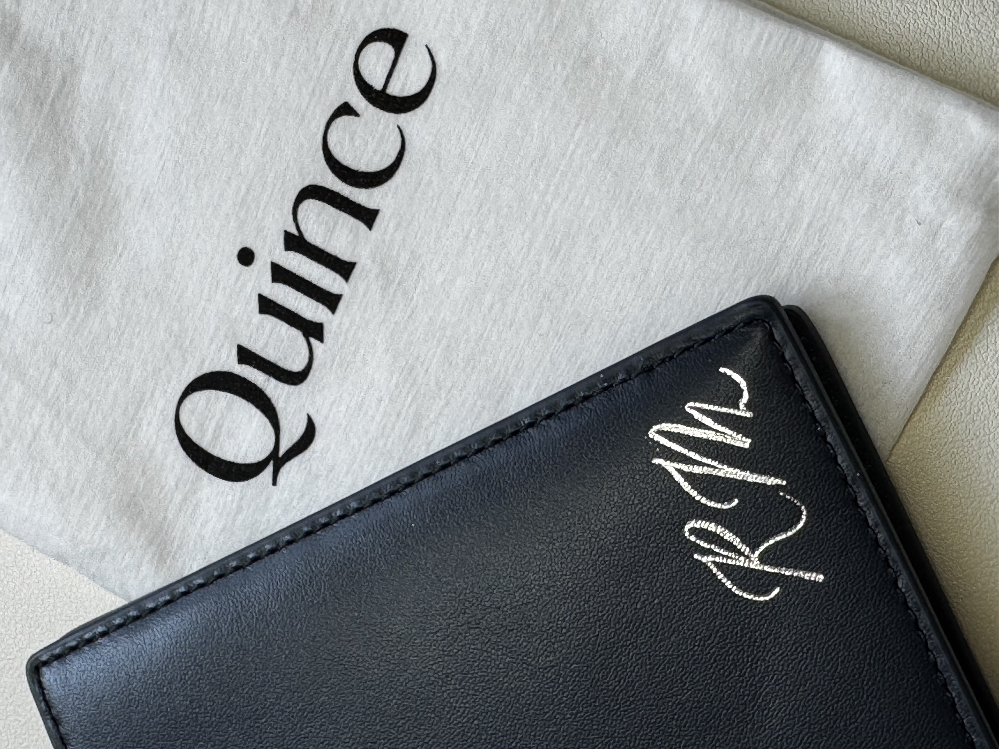 Blue Quince Passport Holder with a personalized RM heat foiled in gold in the bottom right corner laying on top of of a quince bag